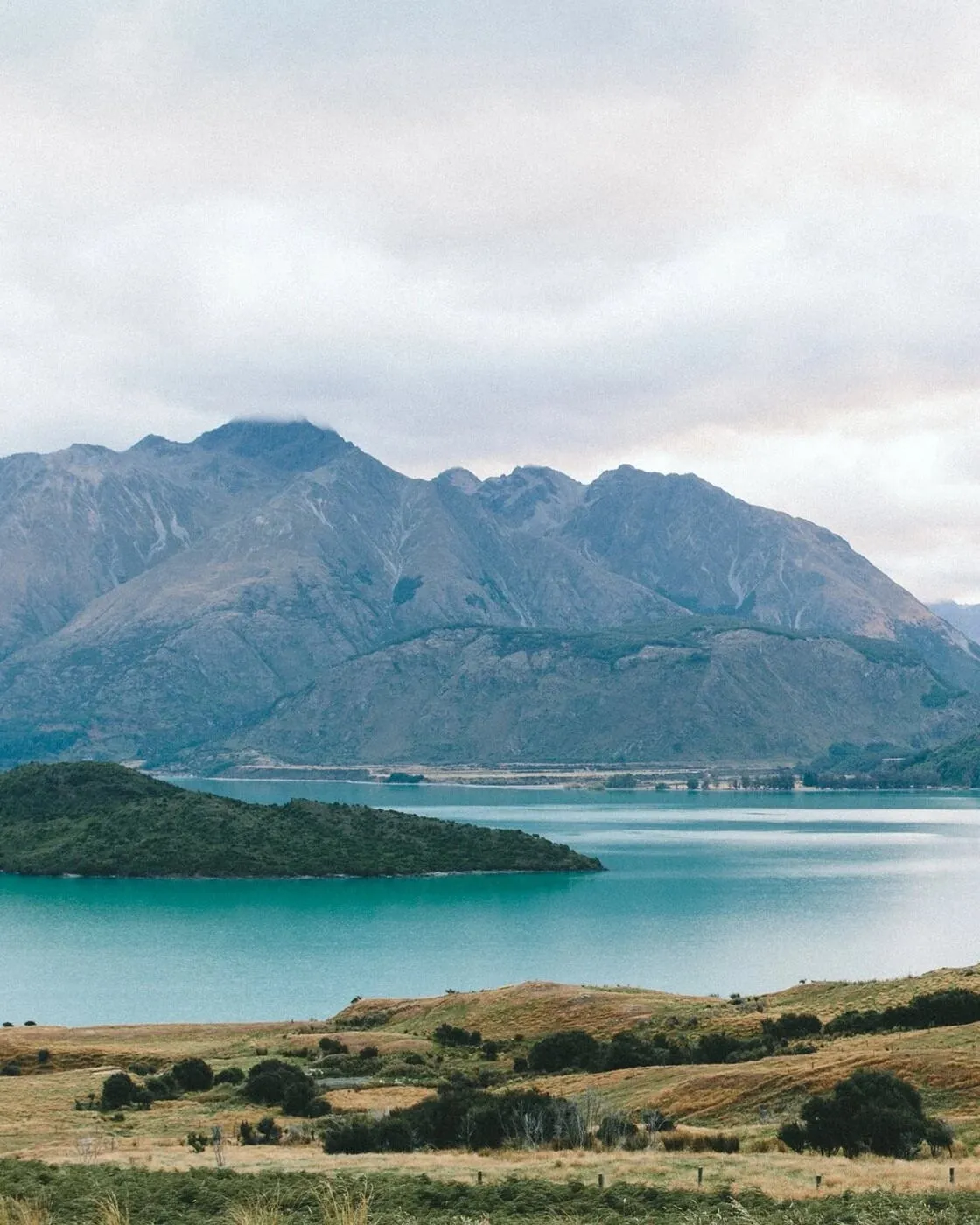 A lake surrounded by green hills and mountains under a cloudy sky.